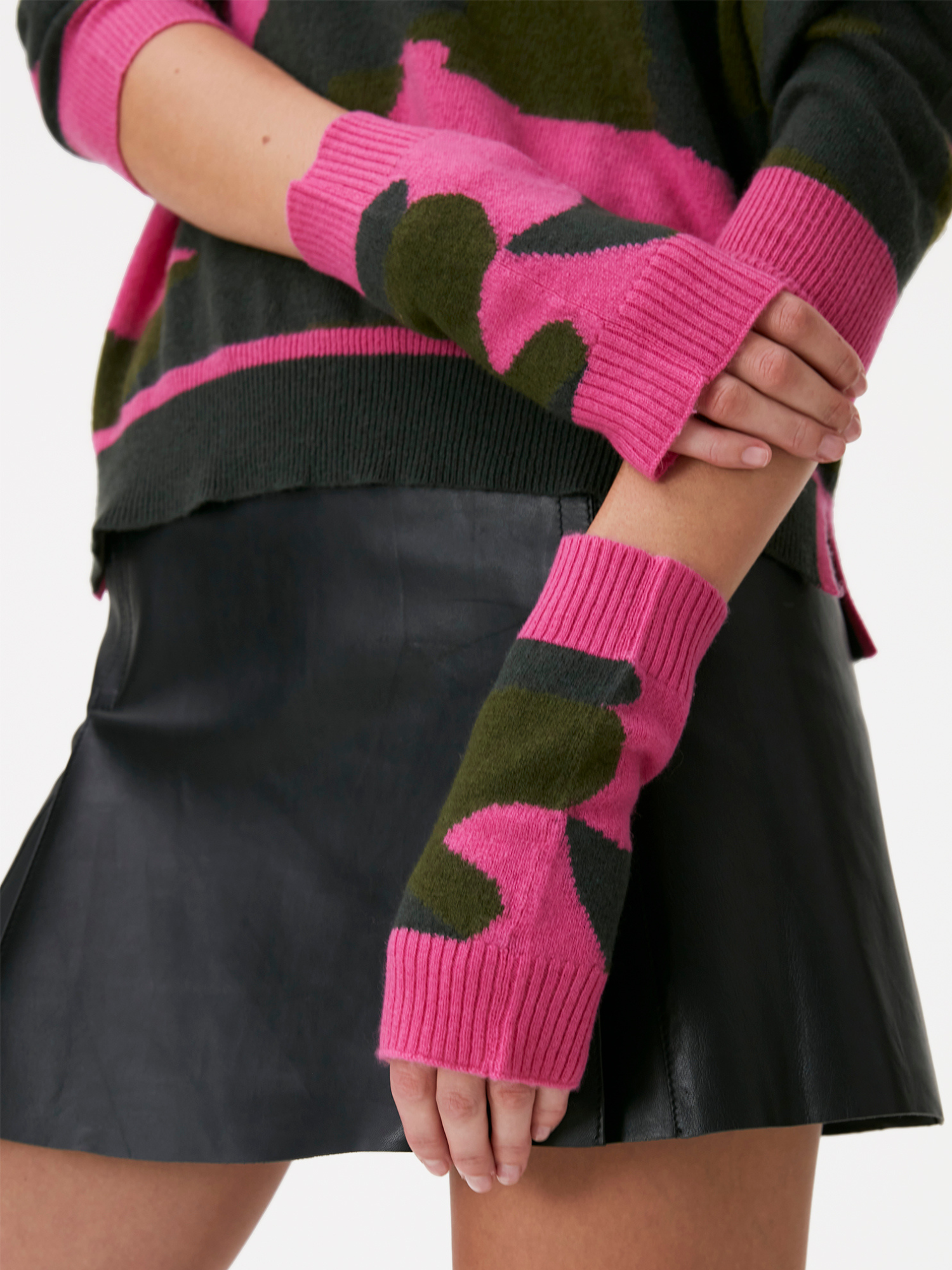 Person wearing pink gloves with green camo patterns, matching sweater, and black skirt.
