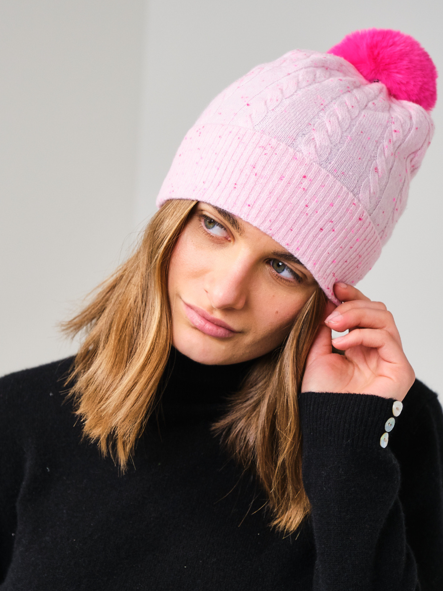 Person wearing a pink knit beanie with a pink pom-pom on a grey background