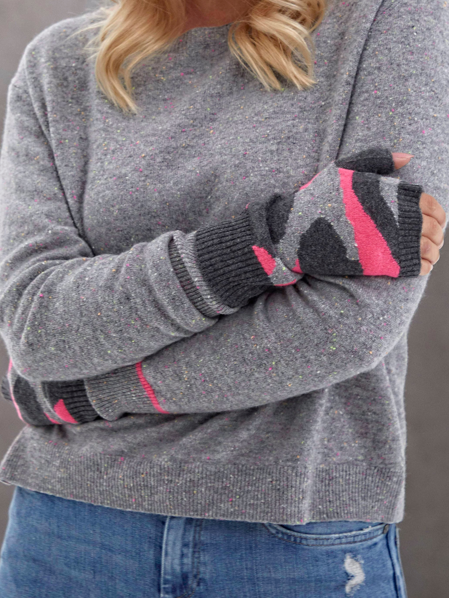 Person wearing a grey sweater with camouflage patterned wrist warmers against a neutral background