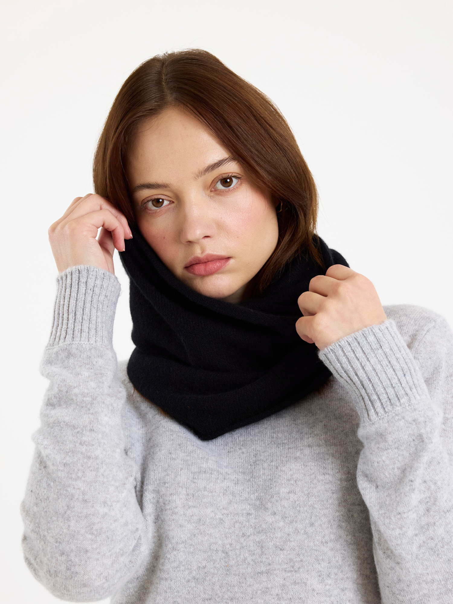 Woman wearing a black snood and grey sweater against a white background